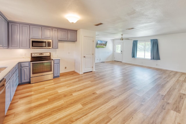 308 Larry Rd, Krugerville, TX 76227 - kitchen with stainless steel appliances, a ceiling fan, light wood-style floors, light countertops, and gray cabinetry