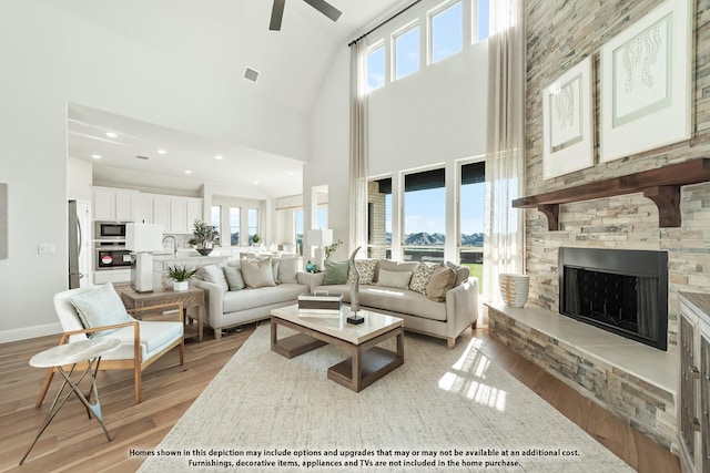 411 Atlas Cedar Dr, Glenn Heights, TX 75154 - living room with light wood finished floors, a towering ceiling, a ceiling fan, a fireplace, and baseboards