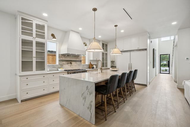 6244 Richmond Ave, Dallas, TX 75214 - kitchen featuring custom exhaust hood, paneled fridge, light wood-type flooring, white cabinetry, and tasteful backsplash
