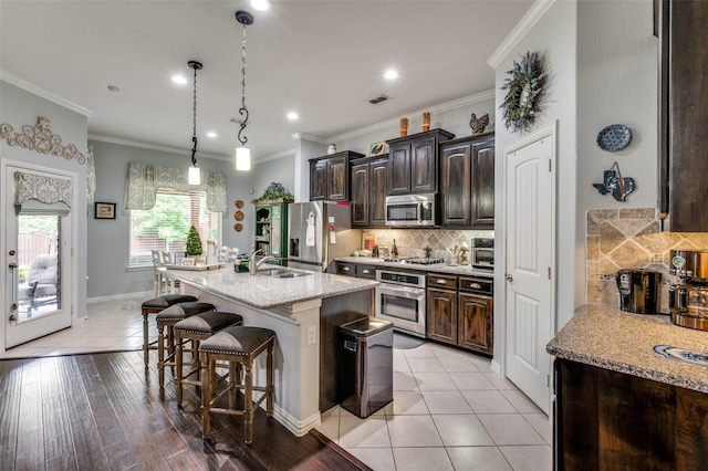 2705 Pioneer Dr, Denton, TX 76210 - kitchen featuring appliances with stainless steel finishes, a sink, a breakfast bar area, decorative backsplash, and dark brown cabinets