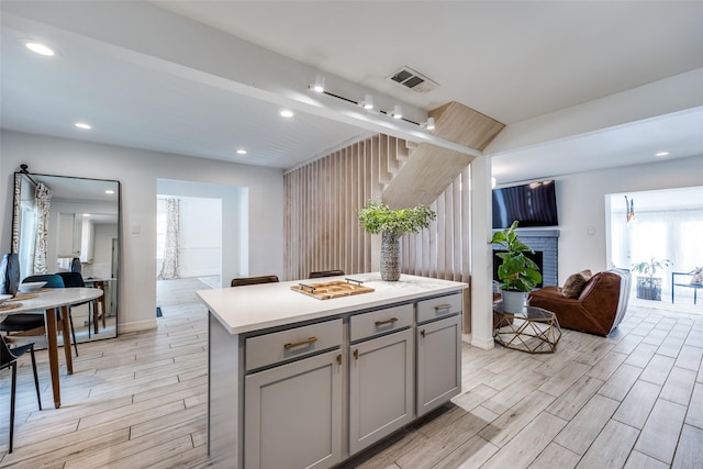 2617 Beechmont Dr, Dallas, TX 75228 - kitchen featuring gray cabinetry, light wood finished floors, a kitchen island, a brick fireplace, and recessed lighting