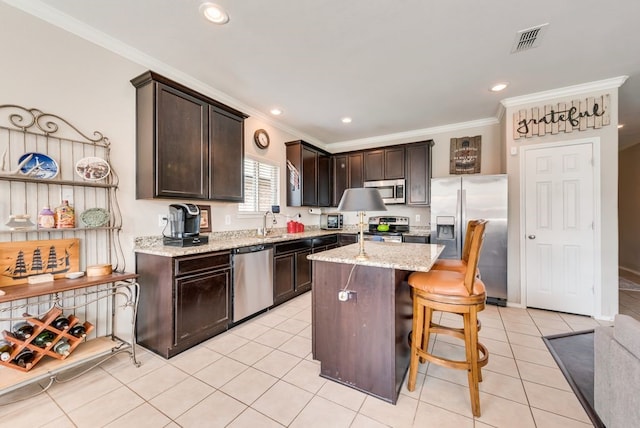 10237 Pyrite Dr, Fort Worth, TX 76131 - kitchen featuring appliances with stainless steel finishes, ornamental molding, dark brown cabinetry, light tile patterned floors, and a kitchen island