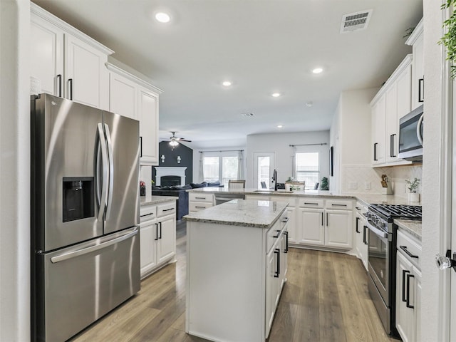 505 Maverick St, Anna, TX 75409 - kitchen featuring appliances with stainless steel finishes, a ceiling fan, a fireplace, a peninsula, and wood finished floors
