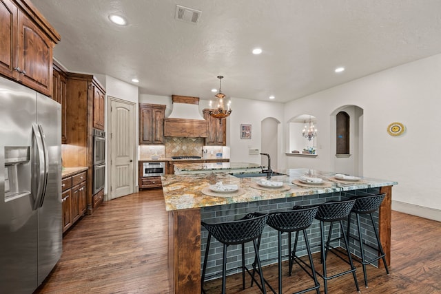 609 Deerwood Ln, Keller, TX 76248 - kitchen with stainless steel appliances, a sink, a large island with sink, premium range hood, and arched walkways
