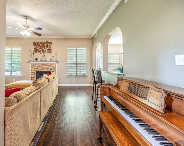 4406 Westcreek Ln, Sachse, TX 75048 - living room featuring ceiling fan, crown molding, arched walkways, dark wood-style floors, and a stone fireplace