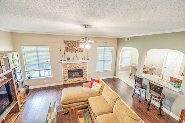 4406 Westcreek Ln, Sachse, TX 75048 - living room with a stone fireplace, arched walkways, hardwood / wood-style floors, a textured ceiling, and ceiling fan