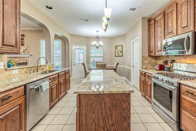 4406 Westcreek Ln, Sachse, TX 75048 - kitchen featuring appliances with stainless steel finishes, a sink, brown cabinetry, arched walkways, and a center island