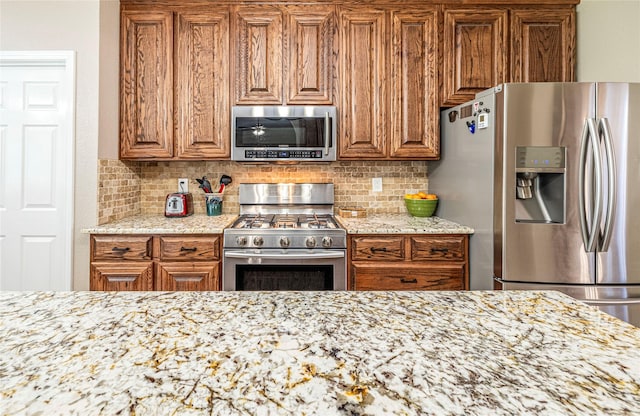 4406 Westcreek Ln, Sachse, TX 75048 - kitchen with stainless steel appliances, brown cabinetry, decorative backsplash, and light stone counters