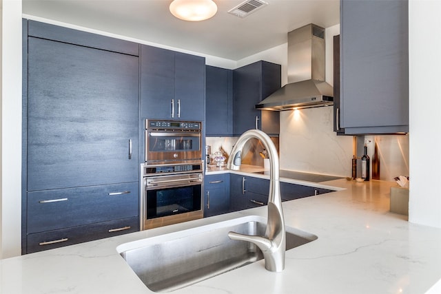 3111 Welborn St Unit 1303, Dallas, TX 75219 - kitchen featuring wall chimney range hood, a sink, double oven, decorative backsplash, and blue cabinets
