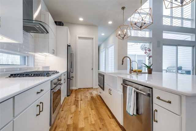 1328 Madeline Pl Unit B, Fort Worth, TX 76107 - kitchen featuring appliances with stainless steel finishes, wall chimney range hood, a chandelier, light wood finished floors, and tasteful backsplash