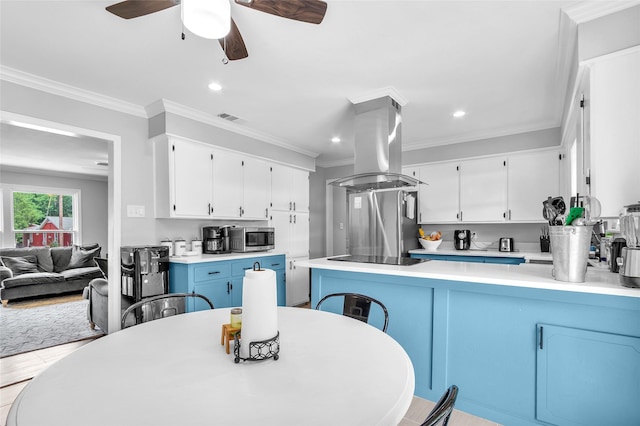 312 Dean St, Athens, TX 75751 - kitchen featuring island exhaust hood, stainless steel microwave, a peninsula, white cabinetry, and crown molding