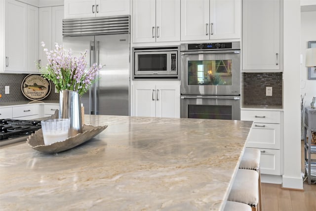 13390 Waterside Dr, Malakoff, TX 75148 - kitchen featuring built in appliances, white cabinetry, light stone countertops, wood finished floors, and decorative backsplash