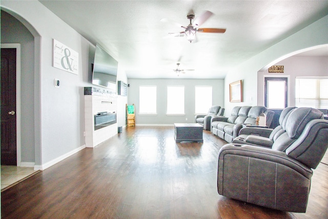 131 Live Oak Ln, Decatur, TX 76234 - living room with ceiling fan, a glass covered fireplace, dark wood-style floors, arched walkways, and baseboards