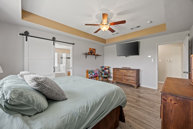 1329 E Highland Rd, Waxahachie, TX 75167 - bedroom featuring a barn door, a tray ceiling, wood finished floors, baseboards, and a ceiling fan