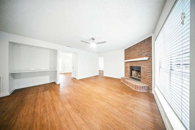 8404 Little Fawn Ln, Dallas, TX 75249 - unfurnished living room featuring light wood-style floors, a brick fireplace, a ceiling fan, a textured ceiling, and baseboards