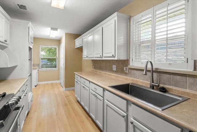 207 Mcmurry Ave, Duncanville, TX 75116 - kitchen featuring range, light wood-type flooring, decorative backsplash, light countertops, and white cabinets