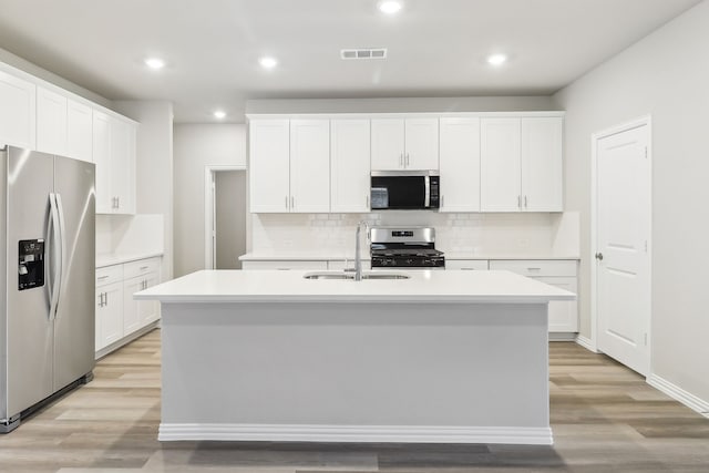 901 Lily Ln, Lavon, TX 75166 - kitchen with appliances with stainless steel finishes, a sink, an island with sink, tasteful backsplash, and light wood-style flooring