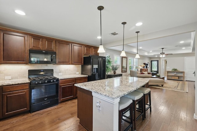 8829 Cantina Bay Ln, Frisco, TX 75036 - kitchen featuring black appliances, hardwood / wood-style flooring, a kitchen island, a kitchen breakfast bar, and decorative backsplash