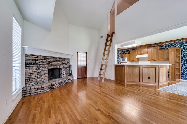 1521 Etain Rd, Irving, TX 75060 - unfurnished living room featuring light wood-style flooring, a brick fireplace, a towering ceiling, and baseboards