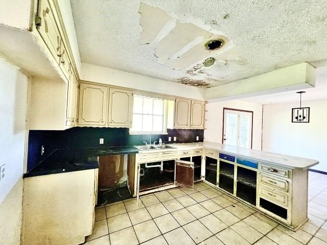 3201 Shoreview Dr, Cleburne, TX 76033 - kitchen featuring a peninsula, a textured ceiling, light tile patterned flooring, a sink, and pendant lighting