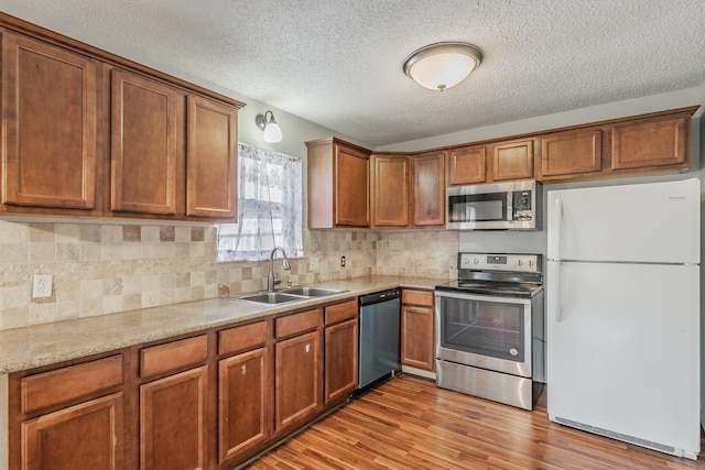 708 Simpson Ter, Bedford, TX 76021 - kitchen featuring appliances with stainless steel finishes, a sink, brown cabinetry, light wood finished floors, and a textured ceiling