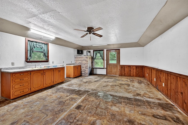 344 Trail Rd, Denison, TX 75021 - kitchen with brown cabinetry, a textured ceiling, ceiling fan, a wainscoted wall, and wooden walls