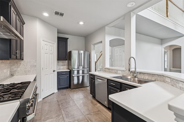 2210 Garden Crest Dr, Rockwall, TX 75087 - kitchen featuring appliances with stainless steel finishes, arched walkways, wall chimney range hood, tasteful backsplash, and light countertops