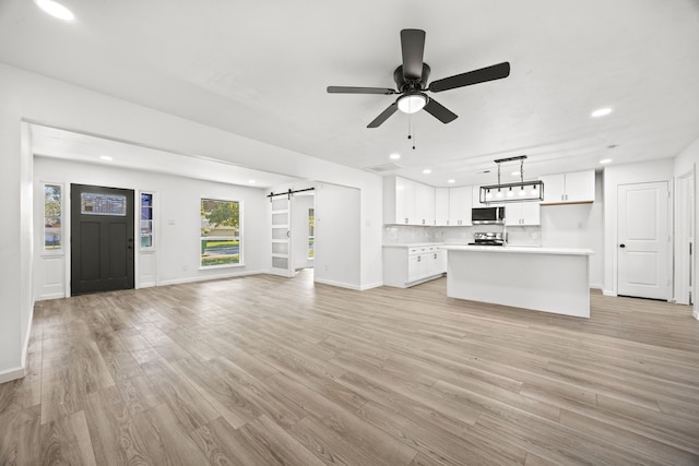 3841 Shady Hollow Ln, Dallas, TX 75233 - unfurnished living room with a barn door, recessed lighting, light wood-style flooring, a ceiling fan, and baseboards