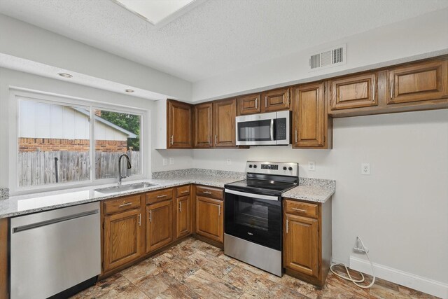 3217 Redwood St, Bedford, TX 76021 - kitchen featuring stainless steel appliances, a sink, brown cabinets, light stone countertops, and a textured ceiling