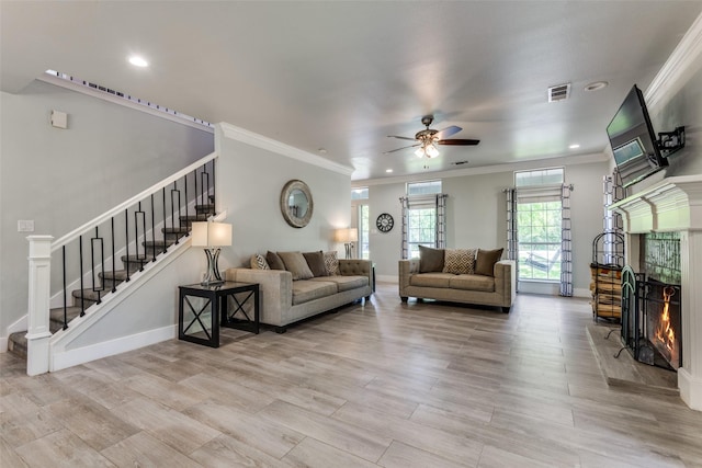 711 Majestic Oaks Dr, Oak Point, TX 75068 - living area featuring a warm lit fireplace, stairway, ornamental molding, a ceiling fan, and light wood-style floors