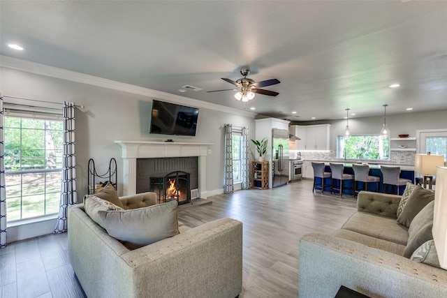 711 Majestic Oaks Dr, Oak Point, TX 75068 - living area with plenty of natural light, a brick fireplace, a ceiling fan, crown molding, and light wood-style floors