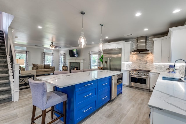 711 Majestic Oaks Dr, Oak Point, TX 75068 - kitchen featuring wall chimney exhaust hood, premium appliances, blue cabinets, light wood finished floors, and white cabinetry
