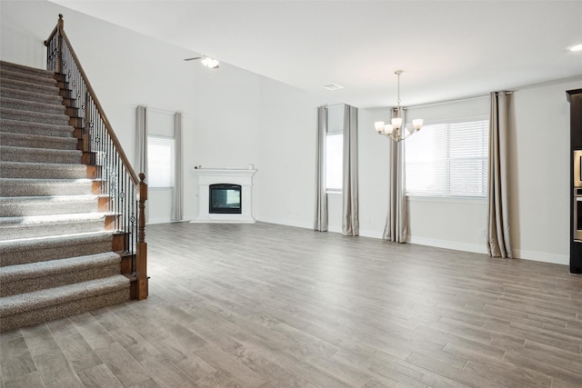 2929 Log Cabin Dr, Celina, TX 75009 - unfurnished living room featuring a chandelier, stairway, wood finished floors, a glass covered fireplace, and baseboards