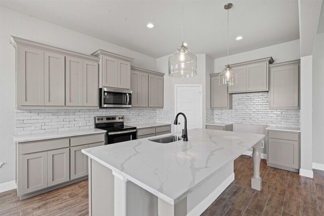 207 Mitchell Dr, Glen Rose, TX 76043 - kitchen featuring appliances with stainless steel finishes, gray cabinetry, backsplash, light stone counters, and a kitchen island with sink