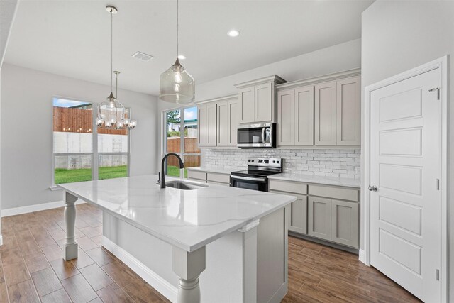 207 Mitchell Dr, Glen Rose, TX 76043 - kitchen with appliances with stainless steel finishes, tasteful backsplash, gray cabinetry, a kitchen island with sink, and dark wood-type flooring