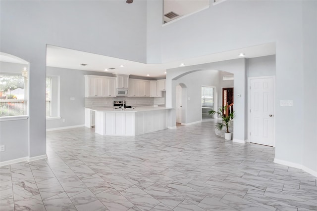5718 Gloucester Dr, Tyler, TX 75707 - unfurnished living room with light marble finish flooring, baseboards, arched walkways, a towering ceiling, and recessed lighting