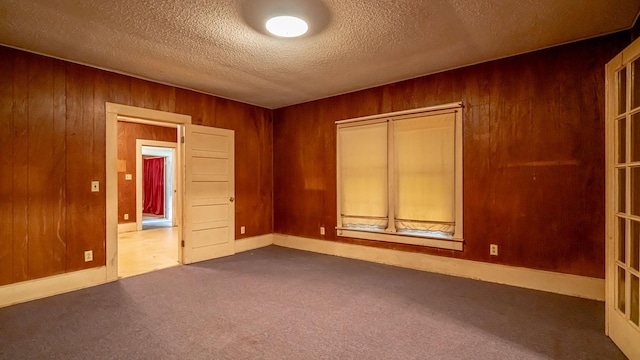 224 Pecan St, Dublin, TX 76446 - empty room featuring dark colored carpet, wood walls, a textured ceiling, and baseboards