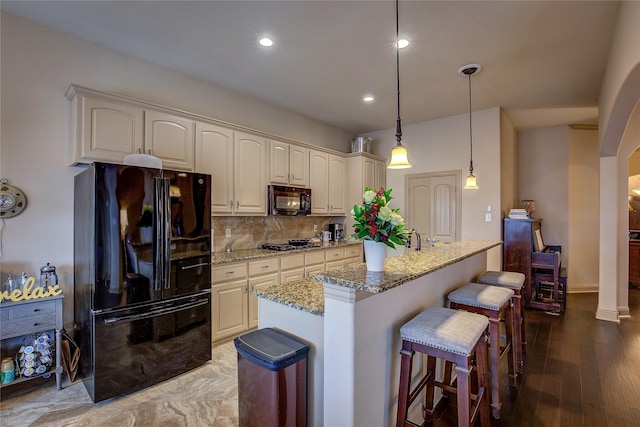189 Charleston Ln, Fate, TX 75189 - kitchen with black appliances, arched walkways, light stone counters, decorative backsplash, and a kitchen breakfast bar