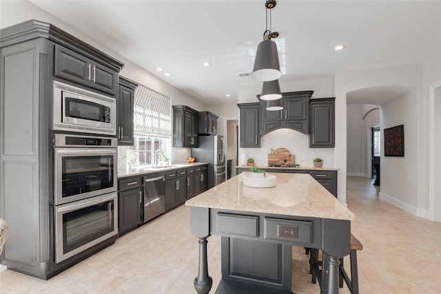 8008 Craftsbury Ln, Mckinney, TX 75071 - kitchen featuring appliances with stainless steel finishes, arched walkways, light stone countertops, tasteful backsplash, and pendant lighting