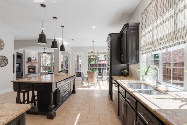 8008 Craftsbury Ln, Mckinney, TX 75071 - kitchen with stainless steel dishwasher, a fireplace, light stone countertops, decorative light fixtures, and stone tile floors