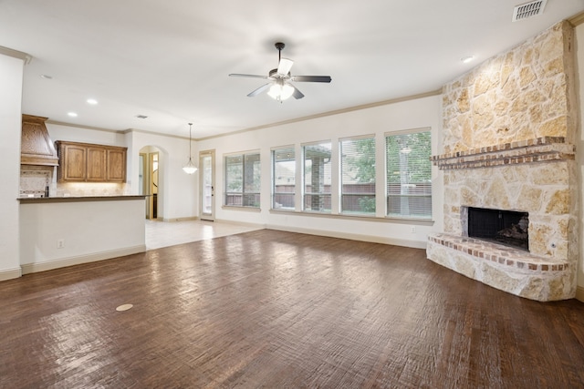 2610 Stonybrook Dr, Prosper, TX 75078 - unfurnished living room featuring a stone fireplace, ceiling fan, arched walkways, ornamental molding, and wood finished floors