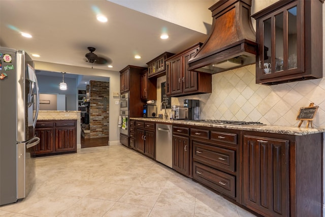 1104 Chesterton Dr, Richardson, TX 75080 - kitchen with custom exhaust hood, stainless steel appliances, a ceiling fan, dark brown cabinetry, and decorative backsplash