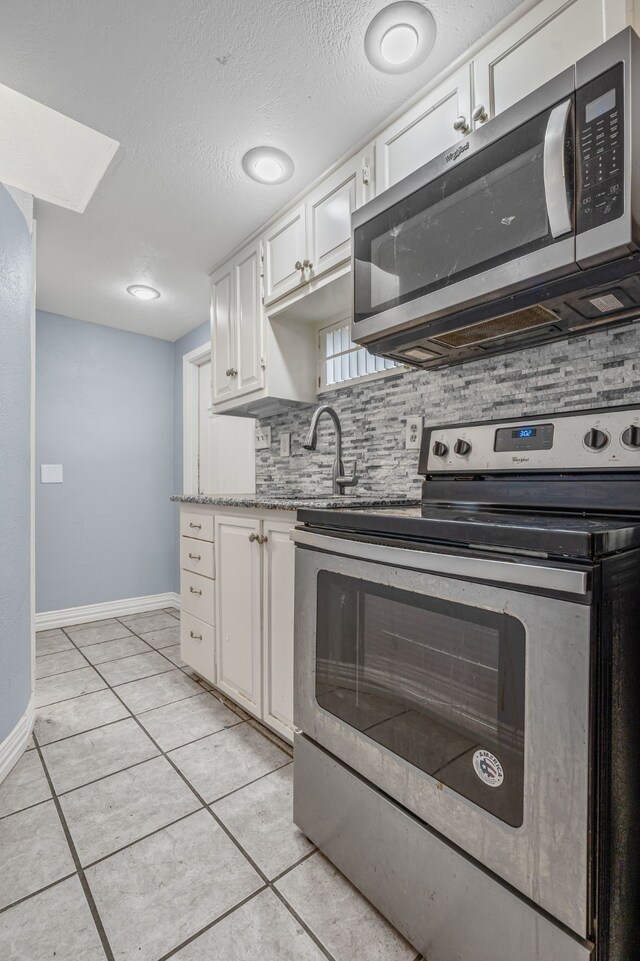 211 Second St, Denton, TX 76201 - kitchen with appliances with stainless steel finishes, tasteful backsplash, white cabinetry, light tile patterned floors, and a textured ceiling