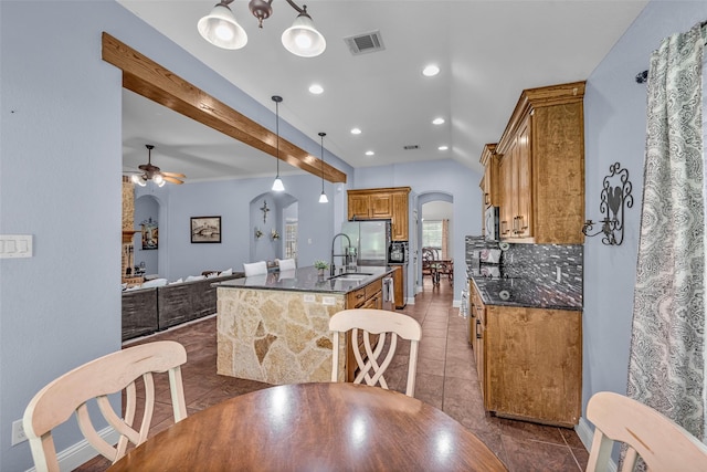 224 Cimmarron Vista Ct, Runaway Bay, TX 76426 - kitchen featuring arched walkways, a kitchen island with sink, a ceiling fan, dark tile patterned floors, and brown cabinets