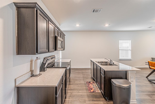 3233 Perman Dr, Mesquite, TX 75126 - kitchen with stainless steel appliances, dark brown cabinets, light countertops, a kitchen island with sink, and dark wood-style floors