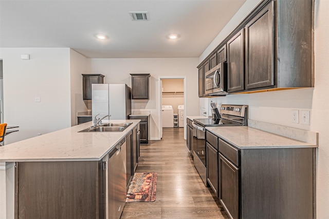 3233 Perman Dr, Mesquite, TX 75126 - kitchen with appliances with stainless steel finishes, washer and dryer, wood finished floors, a kitchen island with sink, and dark brown cabinets