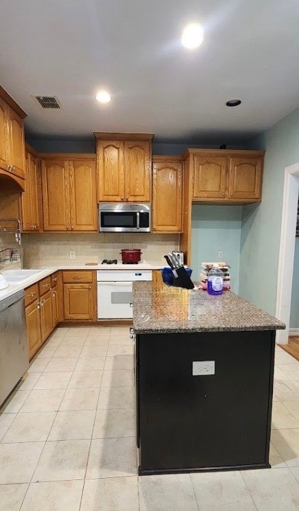 1005 W Bluff St, Fort Worth, TX 76102 - kitchen featuring appliances with stainless steel finishes, tasteful backsplash, light stone countertops, brown cabinetry, and recessed lighting