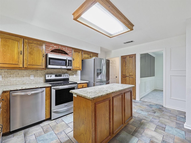9101 Westwood Shores Dr, Fort Worth, TX 76179 - kitchen featuring stainless steel appliances, stone finish flooring, decorative backsplash, a decorative wall, and brown cabinets