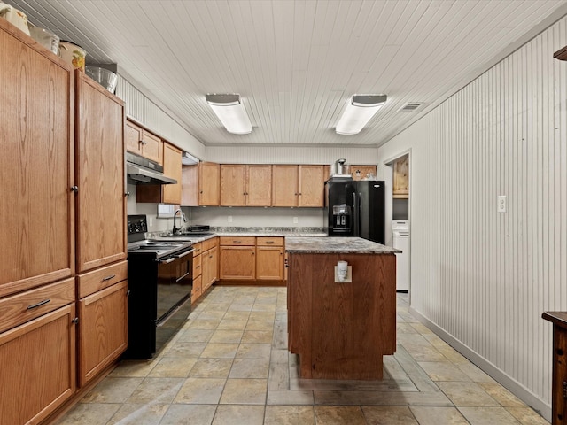 301 Redbud, Ferris, TX 75125 - kitchen featuring black appliances, a kitchen island, under cabinet range hood, and light stone finish floors