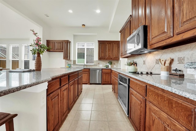 4917 Albatross Dr, Plano, TX 75074 - kitchen with stainless steel appliances, brown cabinetry, backsplash, light tile patterned floors, and light stone counters